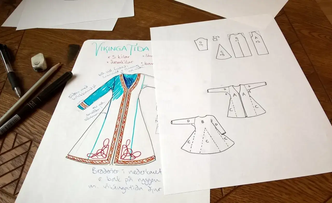 Skisser f&ouml;r en vikingatida dr&auml;kt med m&ouml;nster och s&ouml;mnadsdetaljer. En sy kappa med bl&aring; detaljer och broderier.
