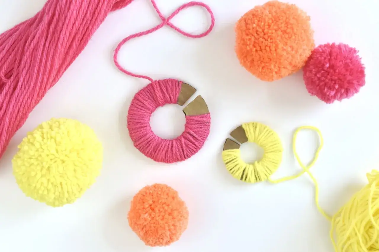 G&ouml;r egna fluffiga pompom med garn i glada f&auml;rger. H&auml;r syns garnnystan, garnlindade mallar och f&auml;rdiga pompom.