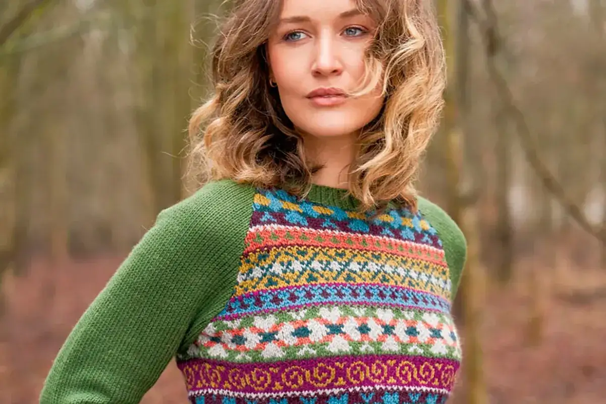 Kvinna med lockigt h&aring;r b&auml;r en gr&ouml;n tr&ouml;ja med f&auml;rgglatt fair isle stickning.