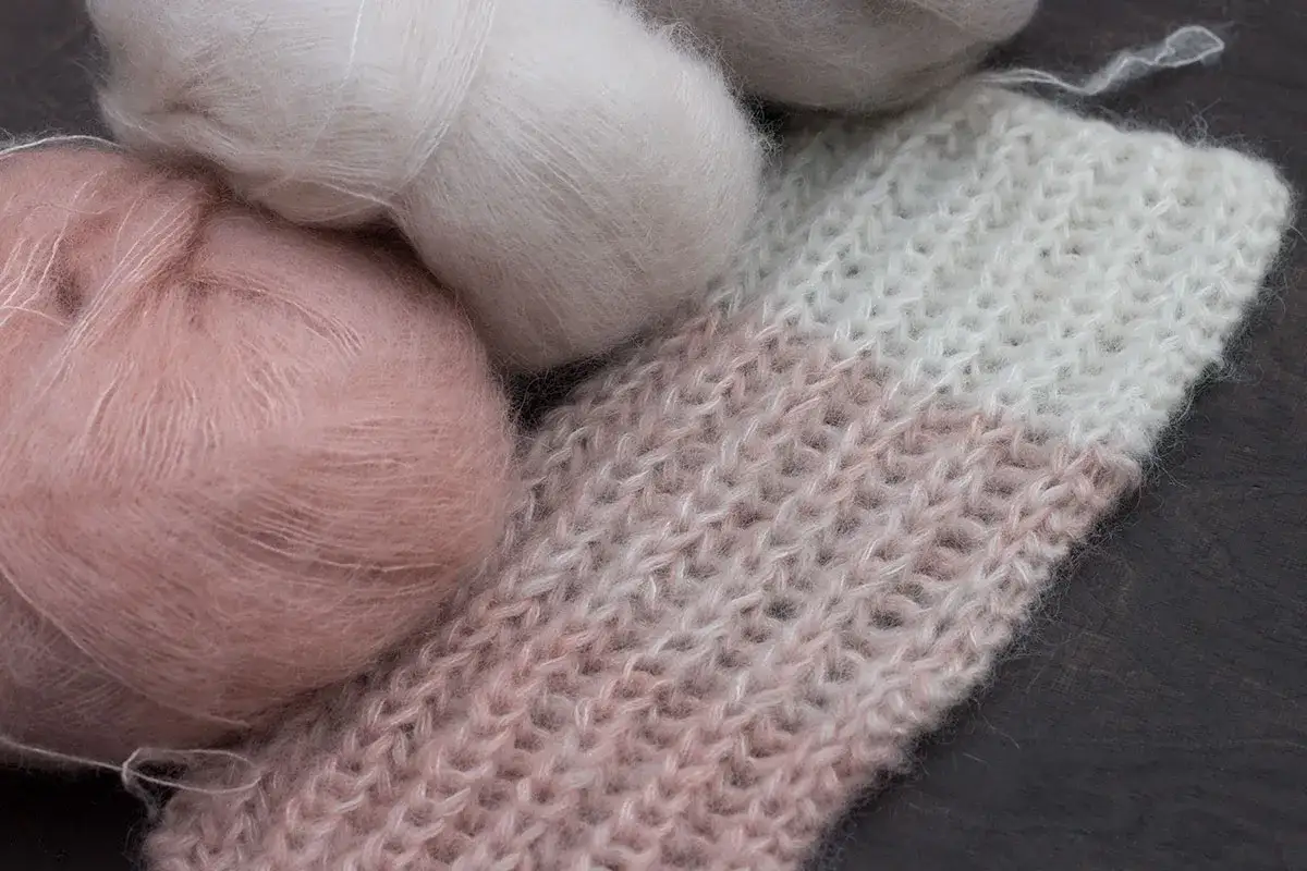 Mjuka garnnystan i rosa och vitt ligger bredvid en stickad filt som h&aring;ller p&aring; att sticka p&aring; rundsticka.