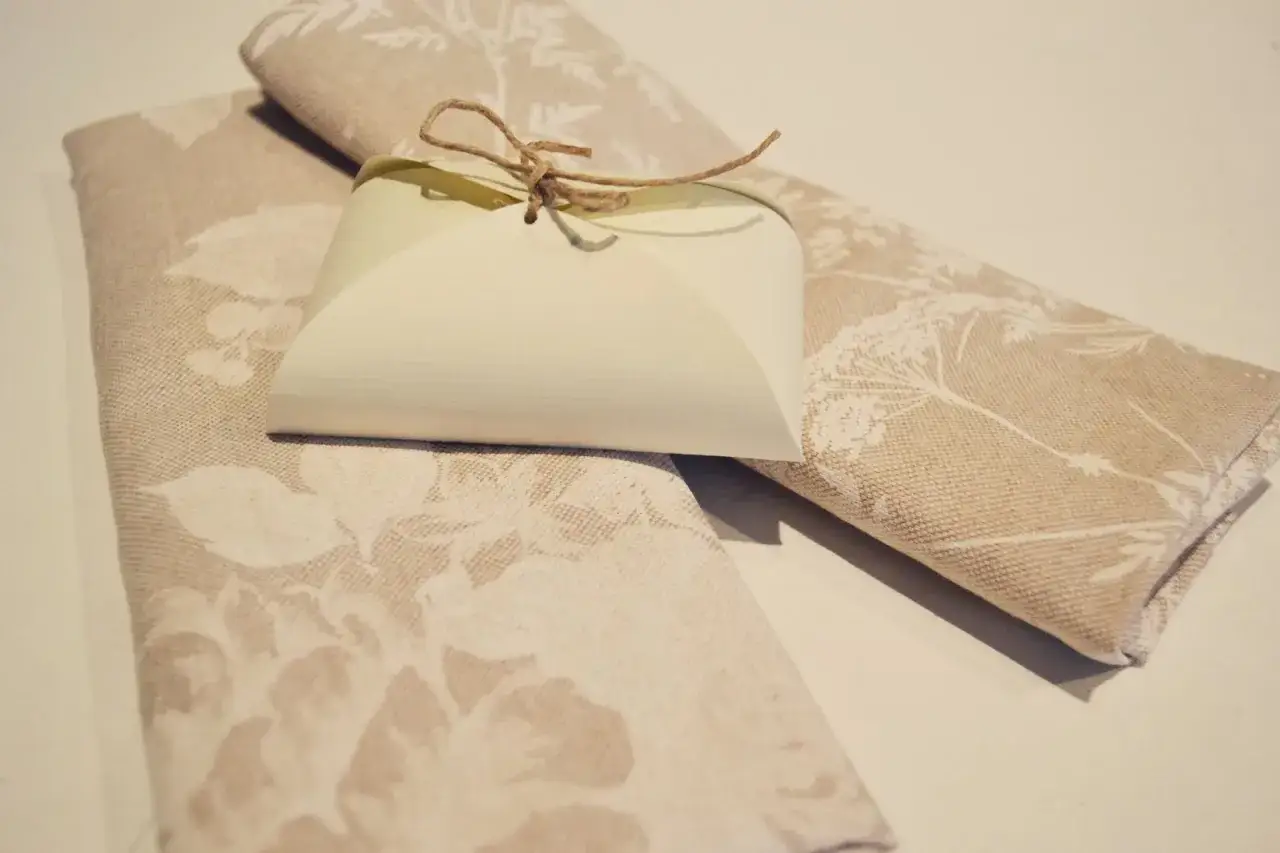 Två tygservetter med blomstermönster, en med en liten presentförpackning bunden med snöre.