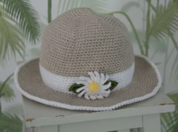 En virkad solhatt för barn, beige med vit kant och en söt blomdekor. Perfekt för soliga dagar!