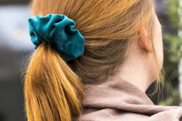 En hästsvans med en turkos scrunchie i sammet. Håret är kopparfärgat och faller mjukt.