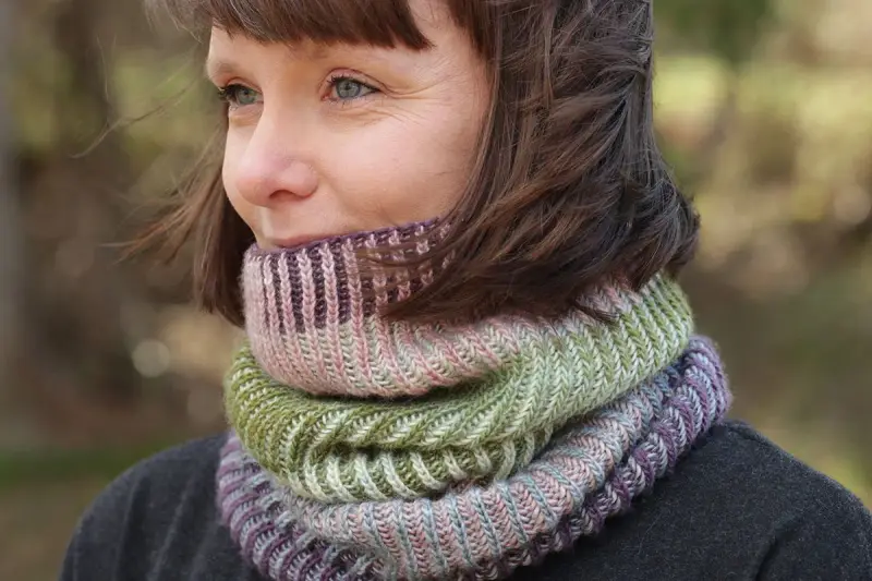 Woman wearing a colorful knitted cowl in shades of green, pink, and purple.